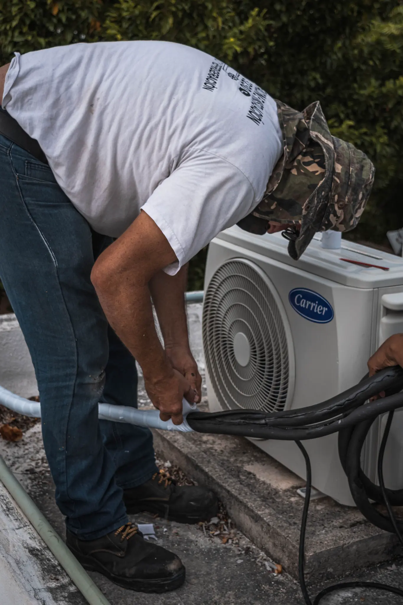 Technician arranging insulated refrigerant lines beside an outdoor condenser